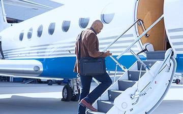 一名肩上背着笔记本电脑包的男性商务旅行者在登上私人飞机的台阶时看着自己的智能手机